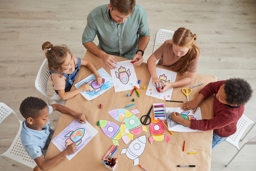 Children and adults collaboratively drawing with crayons at a table in a vibrant day care centers in Frisco.