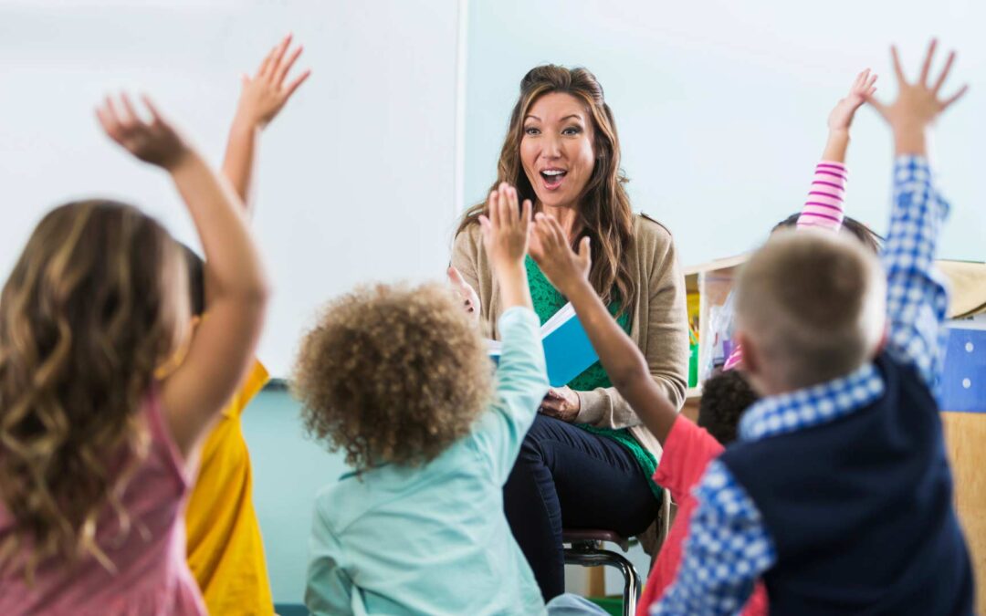 A teacher engages preschool Education Frisco, with students eagerly raising their hands in a vibrant classroom setting.